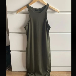 Olivgrön långklänning från Bik Bok - Snygg olivgrön långklänning från Bik Bok med ärmlös design och rund halsringning. Klänningen har en enkel och stilren look, perfekt för dig som gillar minimalistiska outfits. Tillverkad i mjukt och bekvämt material som känns skönt mot huden.