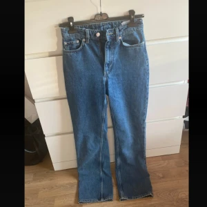 Blå raka jeans  - Klassiska blå jeans med raka ben och hög midja. Jeansen har fem fickor, silverfärgade knappar och är tillverkade i robust denim. Perfekta för en avslappnad och tidlös look.