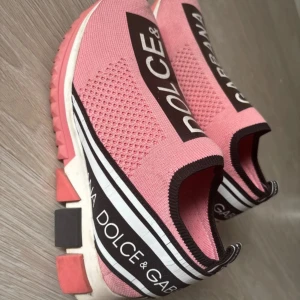  Rosa sneakers - Säljer ett par rosa inspirerad DG sneakers med svart och vit logga längs ovansidan och hälen. Skorna har en sportig design med elastisk ovandel i textil, ventilerande meshpartier och chunky sula i rosa, svart och vitt. Perfekta för dig som vill sticka ut.