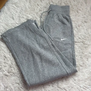 Grå mjukisbyxor från Nike XS - Grå mjukisbyxor från Nike i storlek XS. Byxorna har resår och snörning i midjan, raka ben och en liten vit Nike-logga på ena benet. Tillverkade i mjukt bomullsmaterial för maximal komfort. Perfekta för chill dagar eller träning. Använt någon enstaka gång, originalpris 750kr.