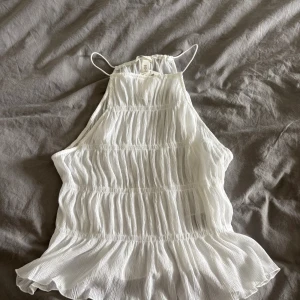 Vit plisserad linnetopp från H&M - Supersöt vit linnetopp från H&M med tunna axelband och plisserad struktur. Toppen har en flowy, volangig nederkant och är tillverkad i ett lätt, luftigt tyg som passar perfekt till varma dagar. Enkel och stilren design som är lätt att matcha. Storlek M
