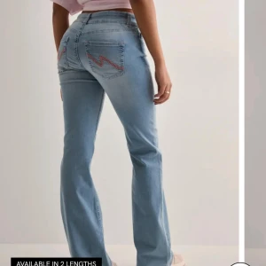 Ljusblå bootcut jeans med broderi - Snygga ljusblå jeans med bootcut passform och klassisk femficksdesign. Jeansen har broderade detaljer i rött på bakfickorna och stängs med knapp och dragkedja. Perfekta för en avslappnad och trendig look.