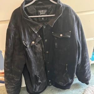 Svart jacka - Svart jacka från Brandit i storlek XL. Jackan har flera fickor med både knappar och dragkedja, klassisk krage och en loose passform. Materialet är troligtvis bomull eller syntet och jackan har en enkel, stilren look med matta metalldetaljer. DEN ÄR INTE SMUTSIG DET ÄR BARA DESIGNEN