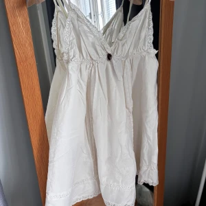 Vit spetsklänning Odd Molly - Supersöt vit kortklänning från Odd Molly med tunna axelband, spetsdetaljer och broderier nertill. Klänningen har v-ringning med liten rosett framtill och är gjord i mjuk bomull. Kan användas som vanlig klänning eller nattlinne