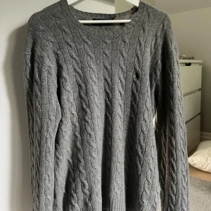 kabelstickad Kashmir tröja från Ralph Lauren - Kabelstickad grå tröja från Ralph Lauren med rund halsringning och diskret broderad logga på bröstet. Tröjan är gjord i ull och Kashmir köpt för ca 2600kr. 