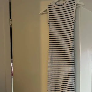 Randig ärmlös klänning i bomull - Snygg ärmlös klänning med svarta och vita ränder. Modellen är kroppsnära och har rund halsringning. Perfekt för en avslappnad och trendig look. Tillverkad i mjuk bomull som känns skön mot huden.