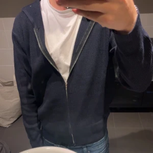 Mörkblå stickad hoodie med dragkedja - Mörkblå stickad hoodie med dragkedja framtill och långa ärmar. Helt ny, aldrig använd