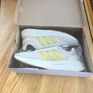 Adidas Cloudfoam sneakers beige/gul - Snygga Adidas Cloudfoam sneakers i beige mesh med gula ränder på sidorna och vit sula. Skorna har snörning och detaljer i syntet, samt en bekväm Cloudfoam Super-sula för extra komfort. Perfekta för dig som vill ha en stilren och sportig look.