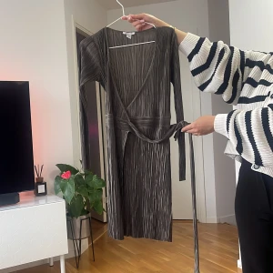 Randig omlottklänning från NAKD - Säljer en snygg randig omlottklänning från NAKD i svart och grått. Klänningen har lång ärm, v-ringning och knytband i midjan för en smickrande passform. Perfekt för dig som gillar stilrena och trendiga plagg.