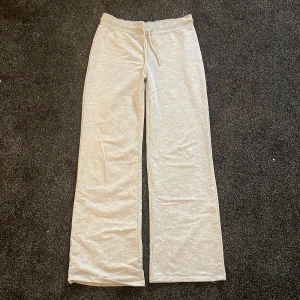 Grå mjukisbyxor från 157, storlek M - Ljusgrå mjukisbyxor från 157 med raka ben och dragsko i midjan. Byxorna är tillverkade i mjukt bomullsmaterial och har en avslappnad passform som är perfekt för chill dagar. Klassisk look med elastisk midja och enkel design.