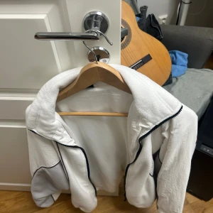 Vit fleecejacka från Iets Frans - Säljer en vit fleecejacka från Iets Frans i storlek M. Jackan har svarta detaljer längs dragkedjan och grå partier på ärmarna. Den är långärmad och har en sportig vibe med mjukt material som passar perfekt till kyliga dagar.