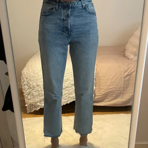 Ljusblå raka jeans med rå kant - Säljer ett par ljusblå jeans med hög midja och raka ben. Jeansen har en klassisk femficksdesign och rå, fransig kant nertill för en trendig look. Perfekta för dig som gillar en avslappnad men stilren vibe.