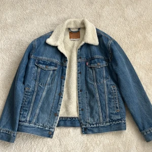 Levi's jeansjacka med teddyfoder  - Säljer en klassisk blå jeansjacka från Levi's med vitt teddyfoder och krage. Jackan har två bröstfickor med knappar, sidfickor och snygga kontrastsömmar.  
