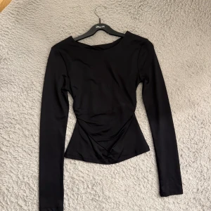 Svart långärmad topp med öppen rygg - Säljer denna supersnygga tröja från Gina med tight passform och en snygg öppen rygg. Toppen har rund halsringning och är tillverkad i ett stretchigt, slätt material som sitter figurnära. Perfekt för dig som vill ha en stilren men ändå unik sexig look.