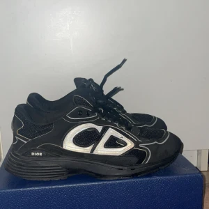 Svarta Dior sneakers med silvriga detaljer - Säljer ett par svarta Dior sneakers med stora silvriga CD-loggor på sidorna och bak. Skorna har snörning, meshpaneler och coola reflekterande detaljer. Snygg chunky sula och sportig vibe, perfekta för dig som gillar statement pieces.