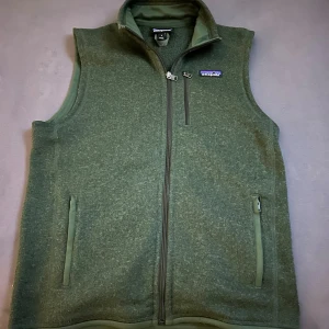 Patagonia väst grön fleeceväst  - Mysig grön fleeceväst från Patagonia med hel dragkedja framtill, två sidofickor med dragkedja och en bröstficka. Perfekt för lager-på-lager och outdoor-vibes. Klassisk ståkrage och diskret logga på bröstet. Har bara använts en säsong pga att den är lite liten på mig