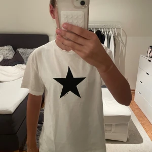 Vit t-shirt med svart stjärna Gina Tricot - Vit t-shirt från Gina Tricot med en stor svart stjärna tryckt på bröstet. Klassisk rund halsringning och korta ärmar. Skön och enkel modell i bomull, perfekt till jeans eller shorts.