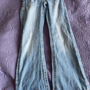 Blå bootcut jeans från Gina Tricot - Snygga ljusblå bootcut jeans från Gina Tricot med dekorativa bakfickor med paljettdetaljer och mönstrad söm. Klassisk femficksmodell i mjukt denimtyg, perfekt för dig som gillar en trendig och avslappnad look.