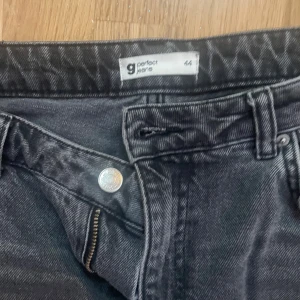 Svarta jeans från Perfect Jeans, strl 44 - Svarta jeans från Perfect Jeans i storlek 44. Klassisk femficksmodell med dragkedja och knapp. Jeansen har en rak passform och slitna detaljer med hål på ena benet för en edgy look. Perfekta för dig som gillar en avslappnad och trendig stil.