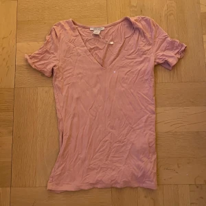 Ljusrosa v-ringad t-shirt  - Säljer en ljusrosa t-shirt från New yorker med v-ringad hals och korta ärmar. T-shirten är gjord i mjuk bomull och har en slim passform som sitter snyggt. Perfekt för dig som gillar enkel och stilren design.