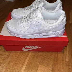 Nike Air Max 90 Triple White sneakers - Fräscha Nike Air Max 90 i helvitt med klassisk chunky sula och snygga detaljer. Ovandelen är i en mix av mesh och skinn med vita snören och diskret Air Max-logga på sidan. Perfekta för dig som gillar stilrena och cleana sneakers.