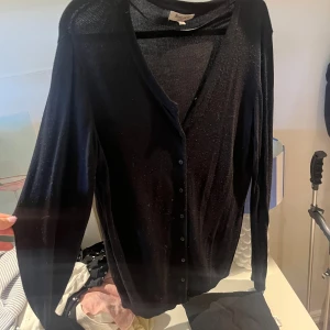 Svart kofta från Basic You, storlek L - Svart tunn kofta från Basic You i storlek L. Koftan har v-ringning, långa ärmar och knäppning framtill med små svarta knappar. Perfekt att slänga över en t-shirt eller linne för en enkel och clean look.