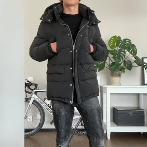 Svart dunjacka från Grifoni - Säljer en svart dunjacka från Grifoni med huva och dragkedja framtill. Jackan har stora fickor med lock och en längre modell som håller dig varm under kalla dagar. Perfekt för dig som gillar en stilren och enkel look.