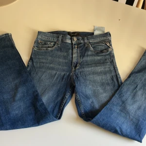 Blå jeans från Replay Thad - Säljer ett par klassiska blå jeans från Replay med raka ben och femficksdesign. Jeansen har snygga kontrastsömmar, läderpatch med Replay-logga bak och är tillverkade i slitstarkt denim. Perfekta för dig som gillar en tidlös och enkel stil.