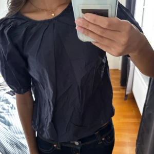 Mörkblå blus från Rodebjer - Säljer en mörkblå blus från Rodebjer med rund halsringning och kort puffärm. Blusen har fina veckdetaljer framtill och resår vid ärmslut och nederkant. 