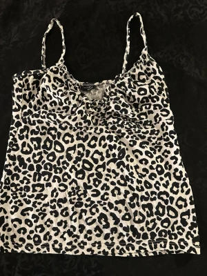 Leopardmönstrad linnetopp från H&M , storlek S - Snygg linnetopp från H&M med leopardmönster i svart och vit . Tunt tyg med smala axelband och lätt rynk vid bysten. Perfekt att styla med jeans eller kjol för en cool look.