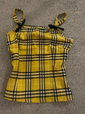 Gul rutig linnetopp från Julie Fashion - Säljer en gul rutig linnetopp från Julie Fashion med svarta och vita detaljer. Toppen har smala axelband som knyts på axlarna och en croppad passform🥰