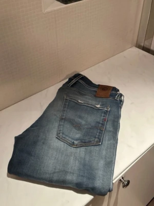 Replay jeans i ljusblå denim - Säljer ett par Replay Grover jeans i ljusblå tvätt med slitningar och snygga detaljer på bakfickorna. Klassisk femficksmodell med läderpatch i midjan och diskret Replay-logga. Jeansen har rak passform och är tillverkade i mjukt denimtyg.