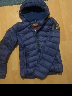 Blå dunjacka från Parajumpers S - Säljer en blå dunjacka från Parajumpers i storlek S. Jackan har luva , dragkedja och en snygg patch på ärmen. Perfekt för kyliga dagar och riktigt skön att bära. Klassisk quiltad look och stilren design.