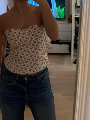 Blommig vit tubtopp med snörning - Supersöt vit tubtopp med små röda blommor och smala axelband som går att ta av. Innersömmen har spruckit lite men det är inget som syns på yttertyget.