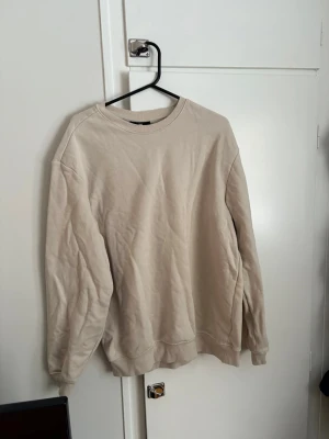 Beige sweatshirt i bomull - Enkel beige sweatshirt med rund hals och långa ärmar. Tillverkad i mjuk bomull och har en relaxed passform. Perfekt för chill dagar eller när du vill ha en clean och stilren look.