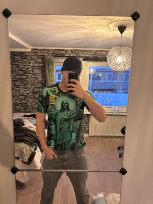 Nike Brasil grafisk t-shirt - Säljer en fet grafisk t-shirt från Nike med Brasil-motiv och stora tryck av Kristusstatyn och coola detaljer. T-shirten är grön och svart med gula accenter och har korta ärmar. Perfekt för dig som vill sticka ut med en unik stil.