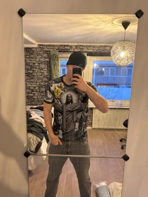 Nike Brasil grafisk t-shirt - Säljer en riktigt fet t-shirt från Nike med Brasil-tema. Den har ett stort grafiskt tryck med Kristusstatyn, änglar och brasilianska detaljer i svart, grått och vitt, samt gula och gröna accenter. Skön passform och tillverkad i mjuk polyester. Perfekt för dig som vill sticka ut.