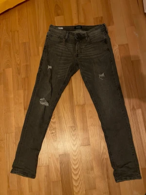 Grå slim jeans från Jack & Jones - Säljer ett par gråa slim jeans från Jack & Jones med slitna detaljer på benen. Jeansen har fem fickor, normal midja och är tillverkade i stretchigt bomullsmaterial för skön passform. Perfekta om du gillar en lite tuffare look.