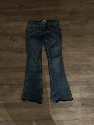 Blå bootcut jeans från Gina tricot - Säljer ett par mörkblå bootcut jeans från Perfect Jeans i storlek 38. Jeansen har klassisk femficksdesign, snygga kontrastsömmar och unika broderade detaljer på bakfickorna. Tillverkade i slitstarkt denim med en skön passform och markerad utsvängd benslut.