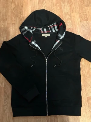 Svart burberry zip - Stilren svart zip-up från Burberry med klassisk och tidlös design. Bekväm passform med dragkedja och exklusiva detaljer som ger en lyxig känsla. Perfekt för både vardag och mer uppklädda outfits.