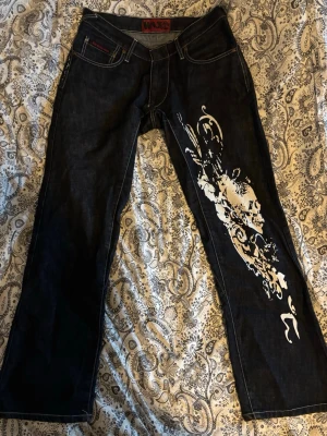 Wax jeans med tryck - Väldigt snygga wax jeans som är väldigt. Knappt täcken på användning förutom en söm som har börjat gått upp men som är oviktig, bara för synens skull, enkelt att fixa. Kolla bilderna! Pris kan diskuteras! 100% bomull, ingen stretch. UNISEX, low/midwaisted. Midjemått: 42cm, Innrebensläng: 80cm