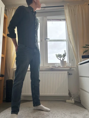 Svart skjorta med knappar från Morris - Säljer en svart skjorta från morris med klassisk krage och vita knappar. Skjortan har lång ärm och en liten broderad logga på bröstet. Snygg och stilren modell som passar till jeans eller chinos.