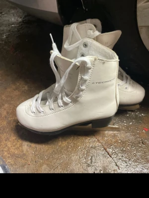 Vita skridskor från Tecnopro - Säljer ett par klassiska vita skridskor från Tecnopro med snörning och rund tå. Skorna har en stilren design i syntetmaterial och är perfekta för dig som vill glida fram på isen med stil. Metallblad undertill och vit ovandel.