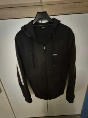 Mörkblå boss hoodie - Stilren mörklbå hoodie med dragkedja och huva. Mjuk och bekväm passform, perfekt för både vardag och avslappnade tillfällen. Klassisk design med diskret BOSS-logga på bröstet. I gott skick.