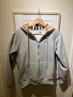 Grå Burberry hoodie  - Säljer denna helt nya burberry hoodien med rutigt tyg i luvan. Riktigt fet tröja att ha nu under vintern och våren. Säljer för att den var för liten när jag köpte och inte hade orken att skicka tillbaka. Behöver pengar så säljer fort. Helt ny utan prislapp 💯💯💯