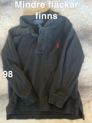 Svart långärmad piké från Polo Ralph Lauren - Klassisk svart långärmad pikétröja från Polo Ralph Lauren med röd broderad logga på bröstet. Skön krage och knäppning framtill. 🌸 Mindre fläckar. Köpt i USA. Storlek 98