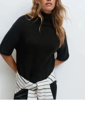 Svart polotröja i stickad ull - Säljer en svart polotröja med korta ärmar i mjuk stickad ull. Tröjan har en hög krage och en croppad passform som ger en modern vibe. Helt ny och använd endast en gång