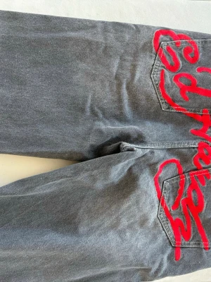 Grå jeans med röd brodyr från Ed Hardy - Unika grå jeans från Don Ed Hardy med stor röd brodyr på bakfickan och mindre broderad logga fram. Klassisk femficksmodell i jeansmaterial med raka ben och cool streetkänsla. Perfekta för dig som vill sticka ut med detaljer och färg.