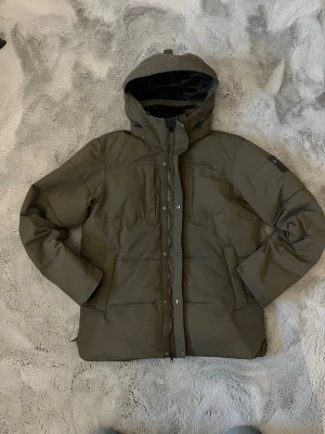 Mörkgrön Vinterjacka - Five Seasons - En mörkgrön vinterjacka ifrån Five Seasons. Den har en justerbar och avtagbar luva. Den är vattentät, vindtät men ändå andningsbar. Köpte den för 2400kr nypris för drygt ett år sedan. Den har ett minimalt hål längst ner vid ena sidan som enkelt går att sy ihop men det syns knappt oavsett. Jag har kvar tagen där står det storlek M, UK 38-40, EU 48-50. Modelen i bild är 189cm och väger 75kg. Vid minsta fråga hör av er, svarar snabbt. 