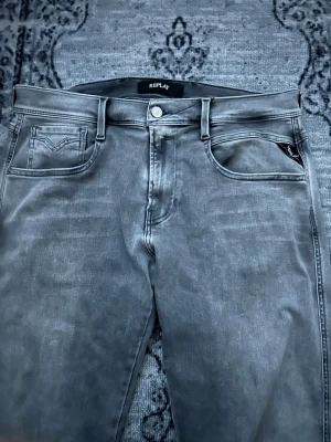 Replay Hyperflex grå jeans  - Säljer ett par grå Replay Hyperflex jeans med klassisk femficksdesign och raka ben. Jeansen har en snygg tvättad look, normal passform och är tillverkade i stretchigt jeansmaterial för extra komfort. Perfekta för dig som gillar stilrena och bekväma jeans.